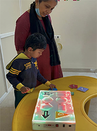 A five year autistic child inserting the shapes on to the device  to learn the basic shapes with the help of  device, which is placed on a table along with the teacher 