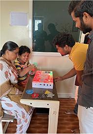 A eight year autistic child inserting the shapes on to the device to learn the basic shapes with the help of  device, which is placed on a table along with the trainer 